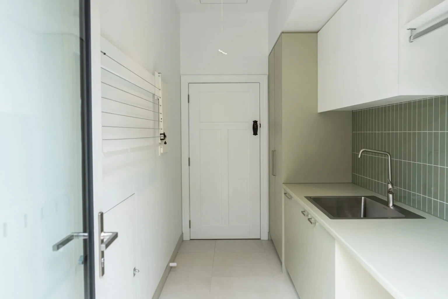 Renovated laundry with green tiled splashback and custom cabinetry in a Melbourne home by Quickset Carpentry