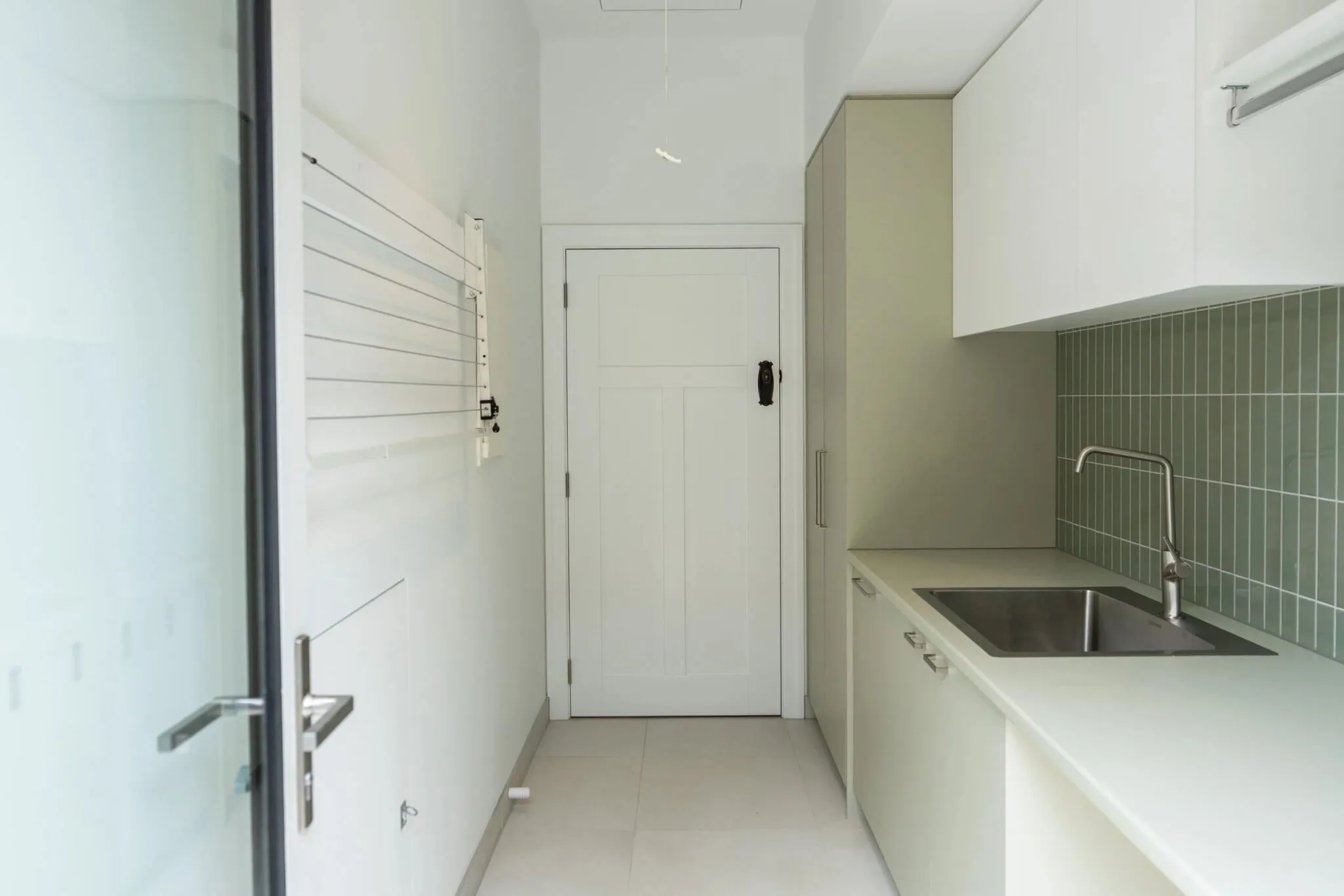 Renovated laundry with green tiled splashback and custom cabinetry in a Melbourne home by Quickset Carpentry