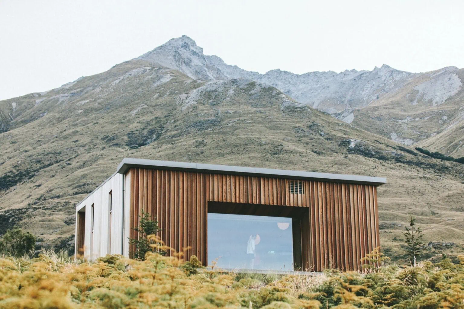 Vertical timber-clad building set against a mountain landscape