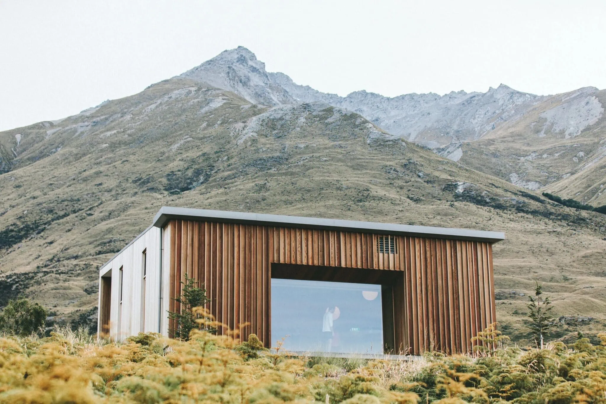 Vertical timber-clad building set against a mountain landscape