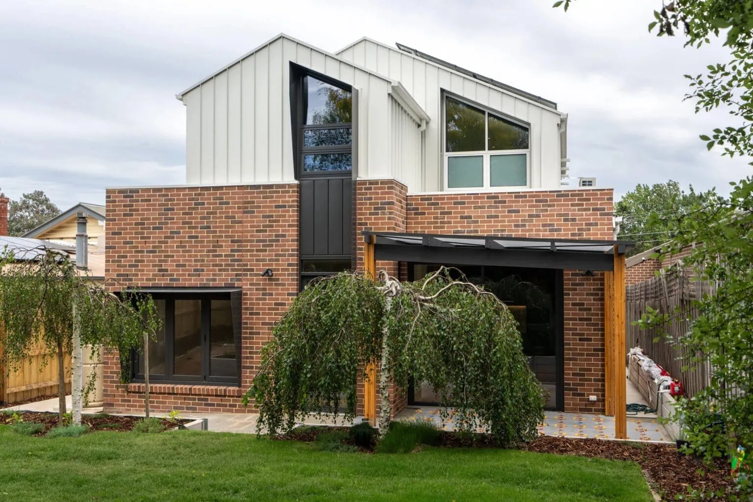 Two-storey rear extension with red brick and white standing-seam cladding on a Melbourne home renovation by Quickset Carpentry